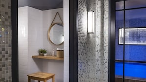 A modern bathroom with white subway tiles, a wooden bench, a mirror, and a shelf with toiletries.