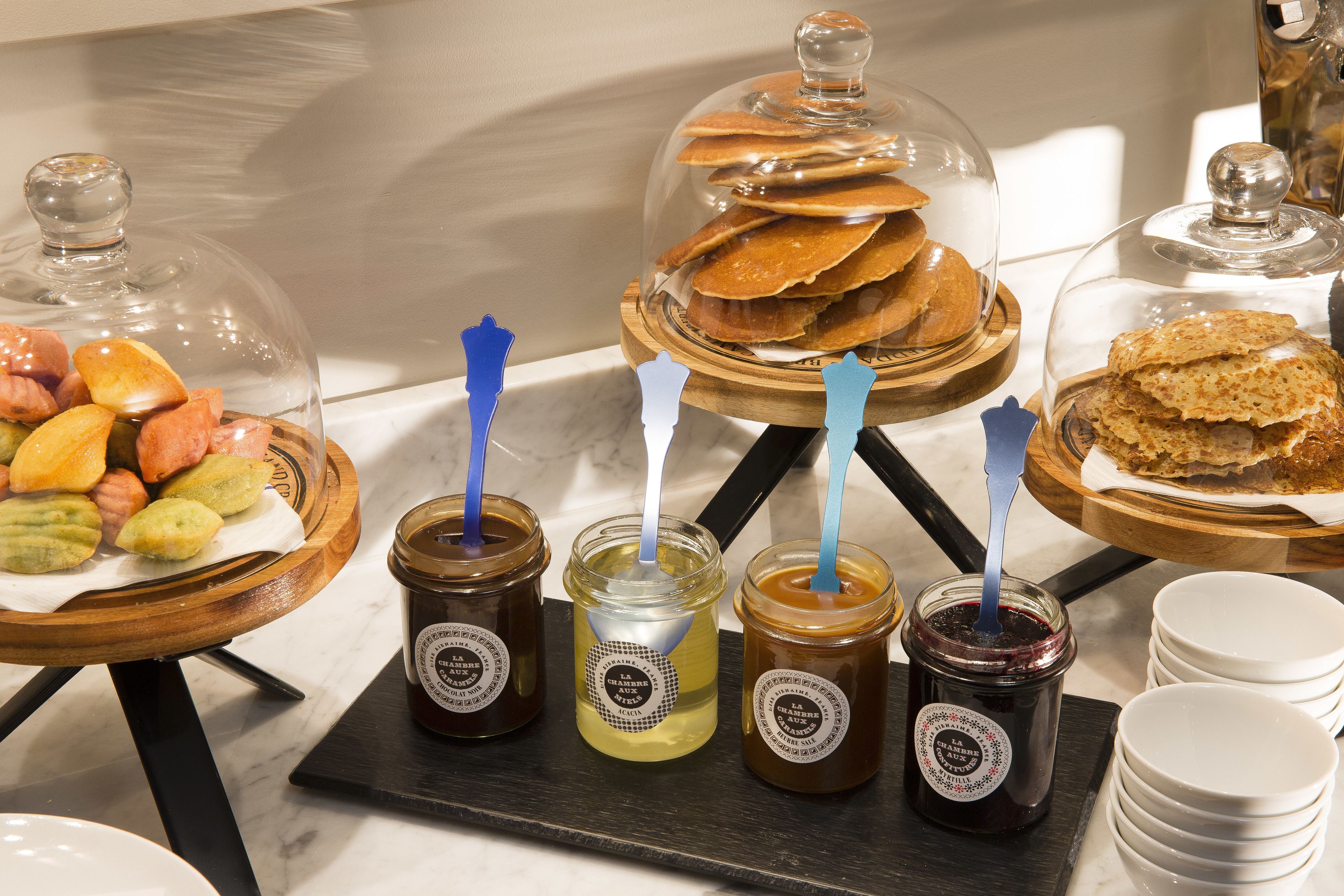 A buffet with various food items and condiments, including pastries under glass domes and jars of spreads.