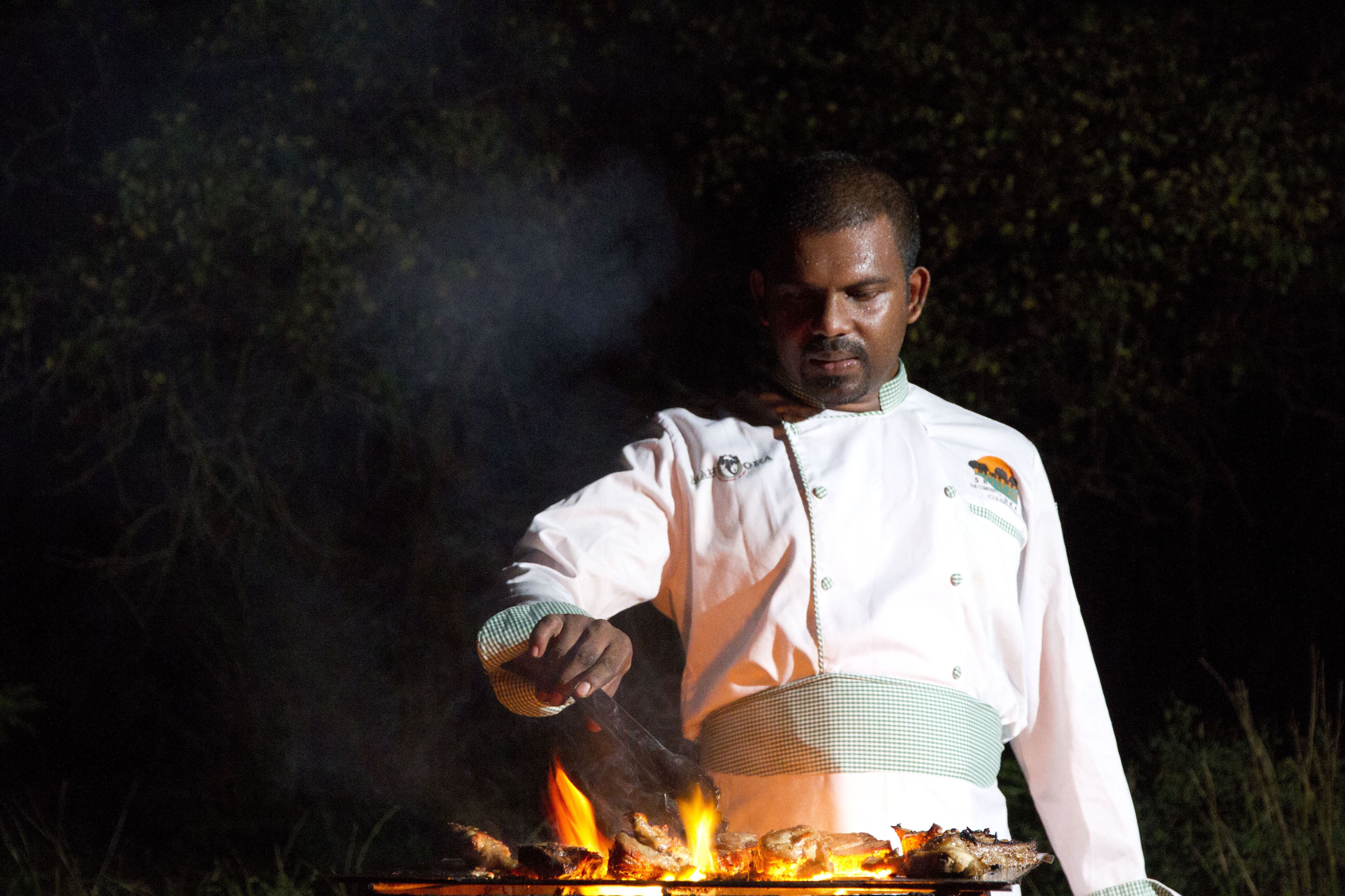 A chef grilling meat outdoors at night.