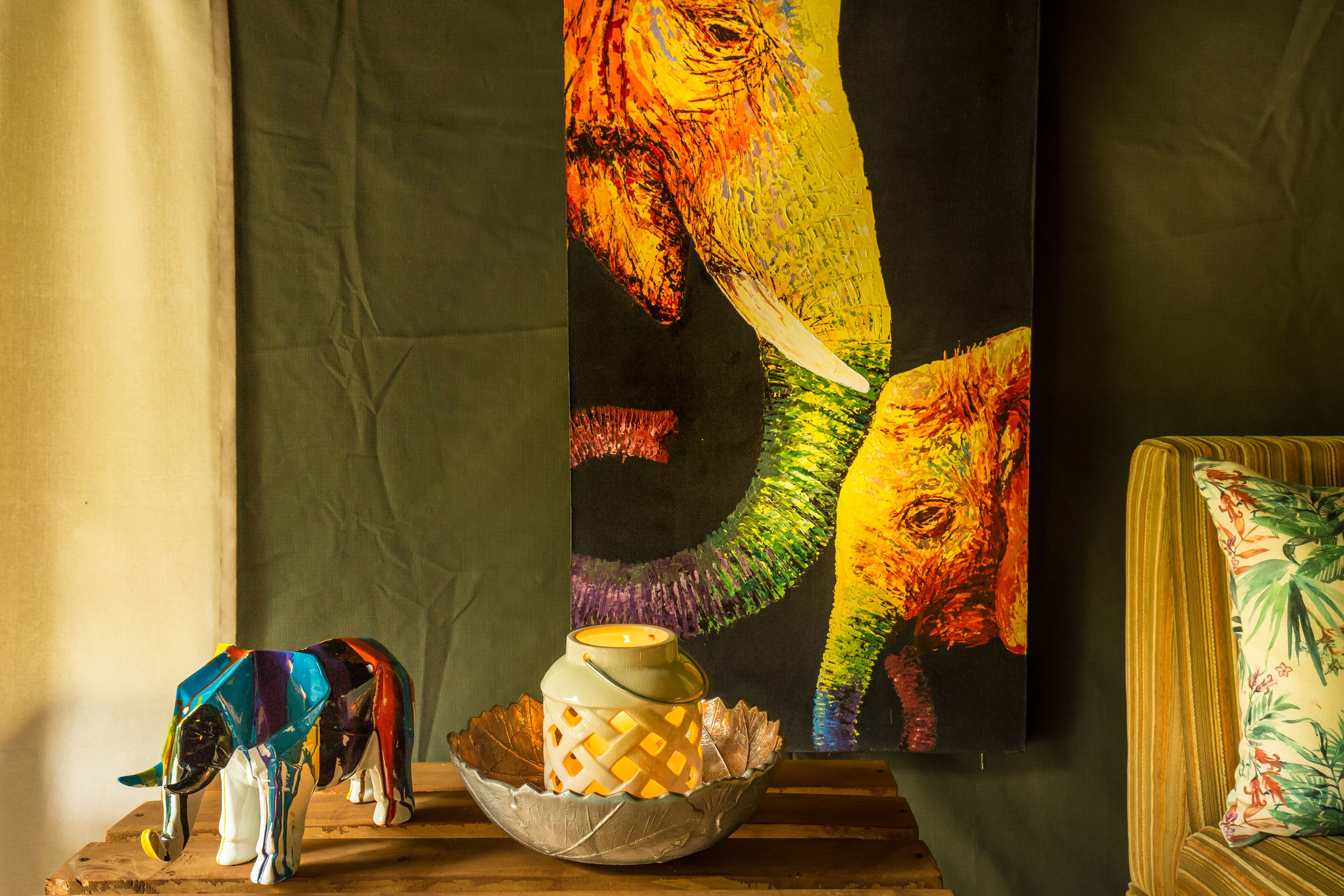 A decorative elephant figurine, a ceramic jar, and a colorful painting of an elephant on a wooden surface.
