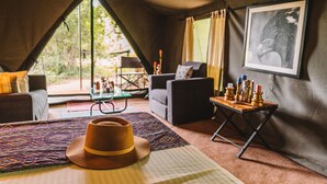 A tented accommodation room with a bed, a table with candles, a sofa, and a framed picture on the wall.
