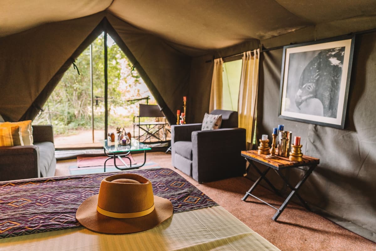 A tented accommodation room with a bed, a table with candles, a sofa, and a framed picture on the wall.