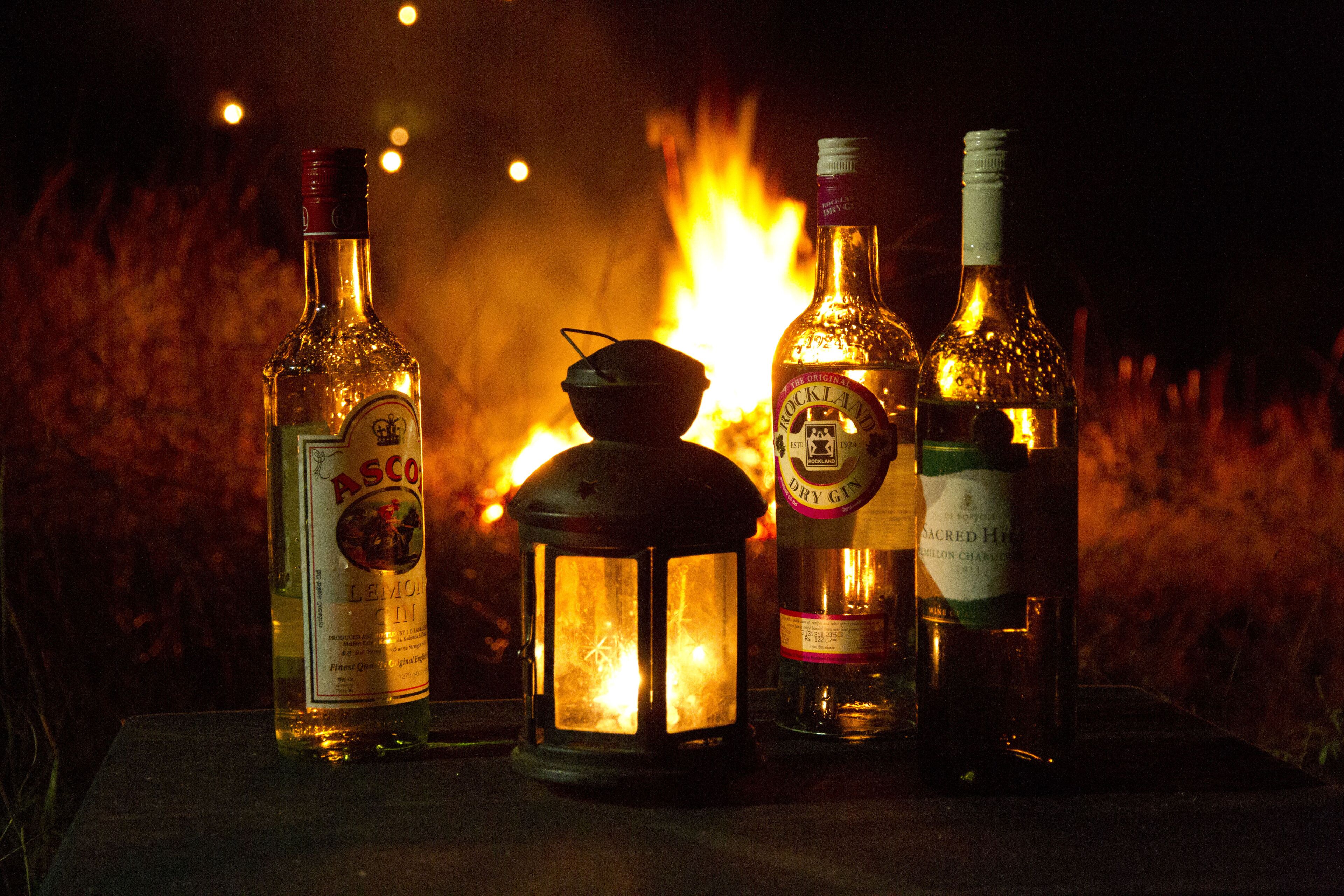 Cuatro botellas de alcohol y un farolillo frente a una fogata.