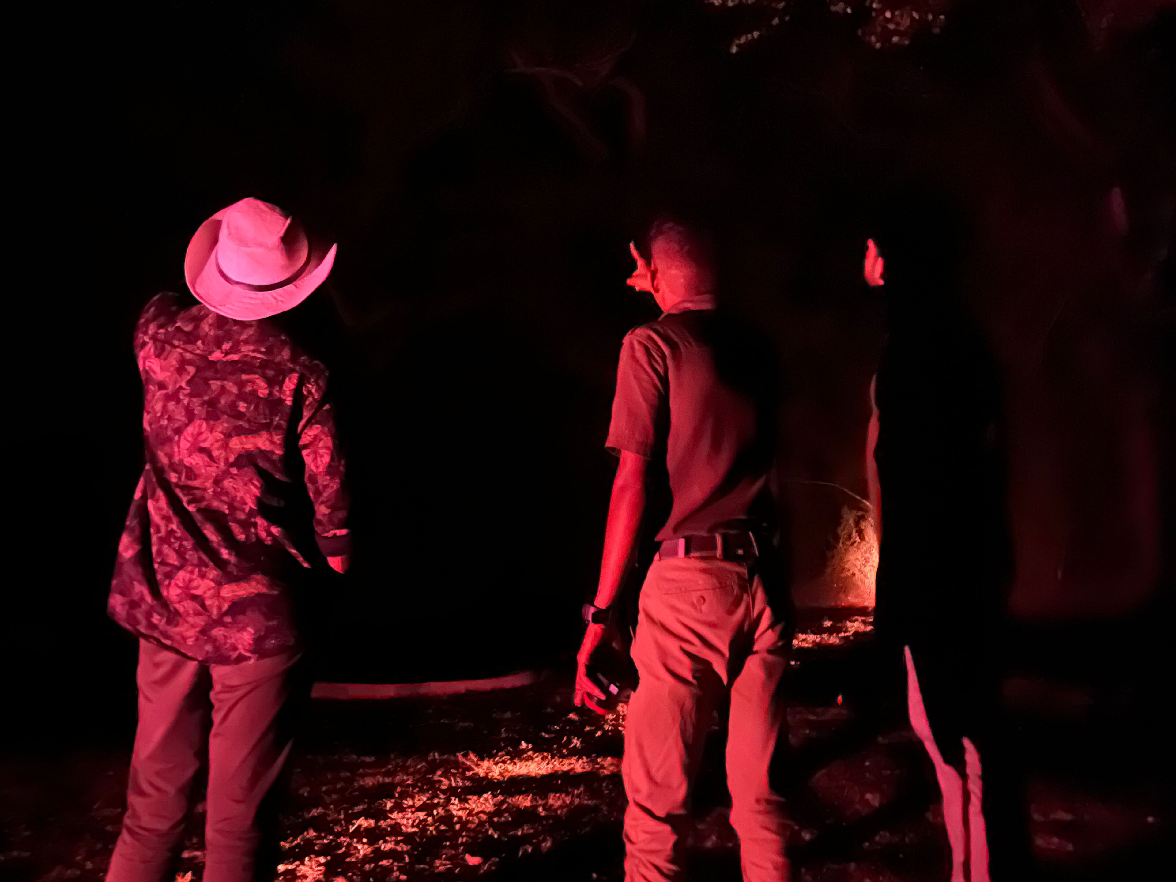 Two individuals standing in a dimly lit area with a fire burning on the ground.