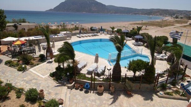 Zona de piscina amb gandules i ombrelles, envoltada de palmeres i una vista al mar i a una muntanya.