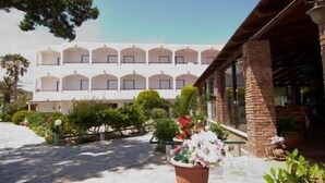 Un hotel amb façana blanca, nombrosos balcons i un pati empedrat de pedra.