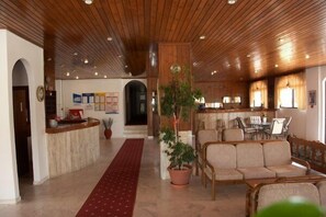 A lobby with a wooden ceiling, a reception desk, a red carpet, and seating area. - Ionikos Hotel (Kos)