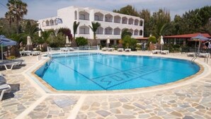 Una piscina amb terrassa de pedra, envoltada de gandules i ombrel·les, i un edifici al fons.