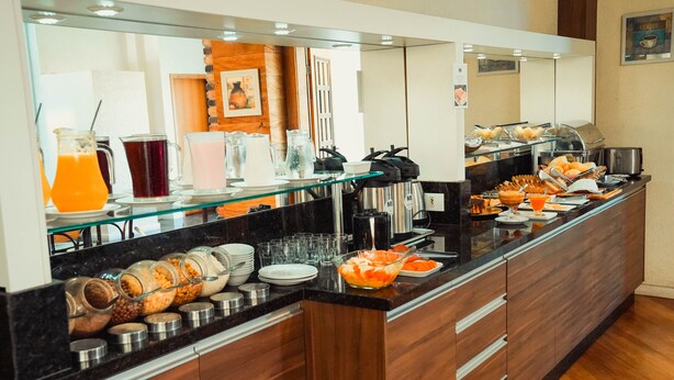 A buffet counter with various food items, beverages, and condiments. - Hotel Imperial (Quatro Barras)