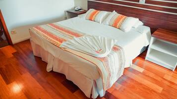 A neatly made bed with a patterned bedspread and pillows, a bedside table with a lamp, and a wooden floor.