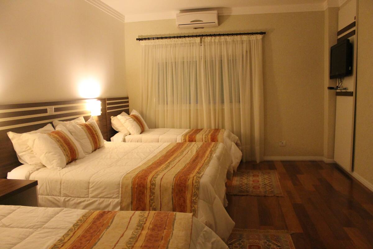 A hotel room with two beds, a television, and a window with curtains.