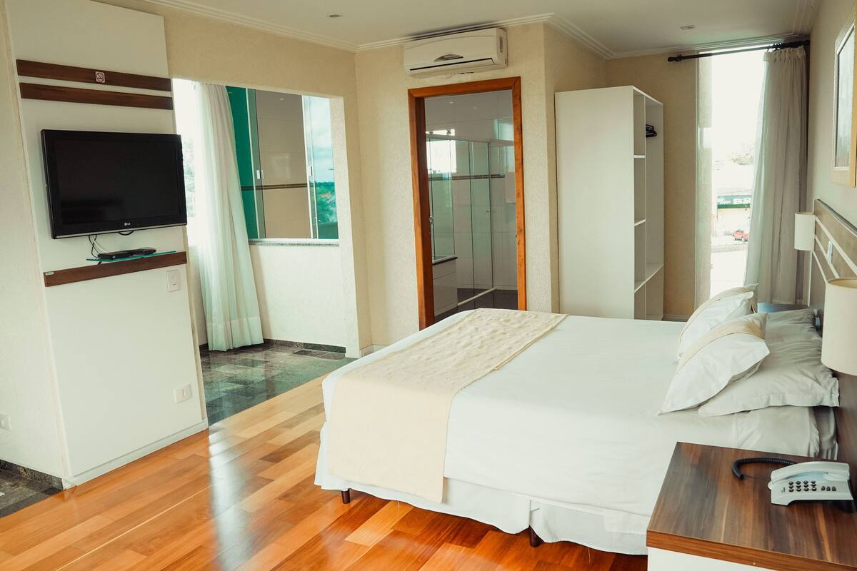 A hotel room with a bed, a TV, a wardrobe, and a bathroom visible through a glass door.