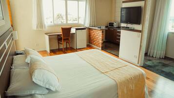 A hotel room with a large bed, a desk with a chair, a small kitchenette, and a TV mounted on the wall.