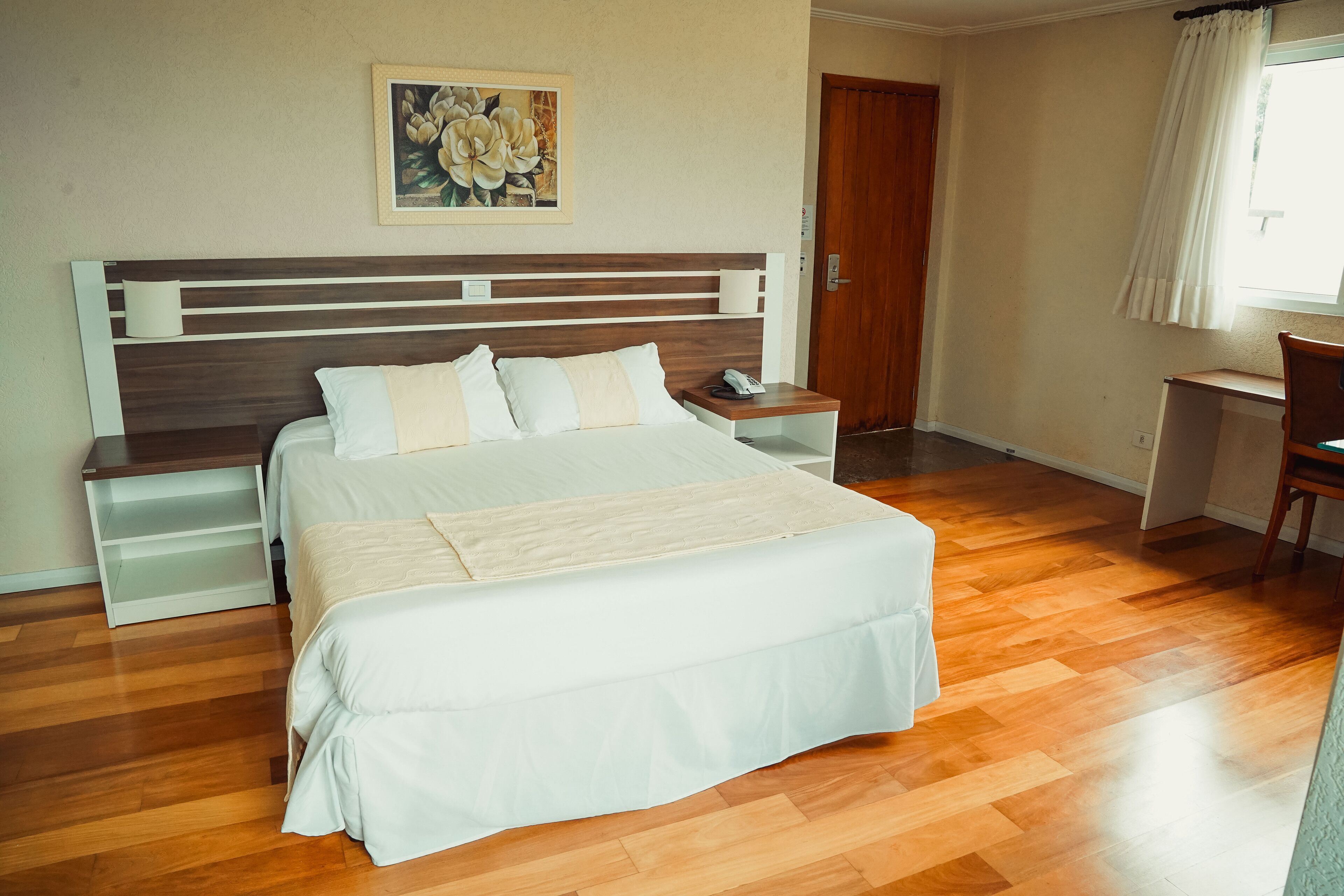 Un dormitorio con una cama de madera, ropa de cama blanca, una mesita de noche con un teléfono, un escritorio y una silla.