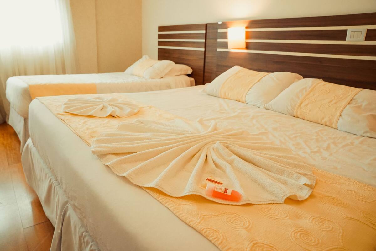 A hotel room with two beds, each with a neatly arranged towel and a bottle of lotion.