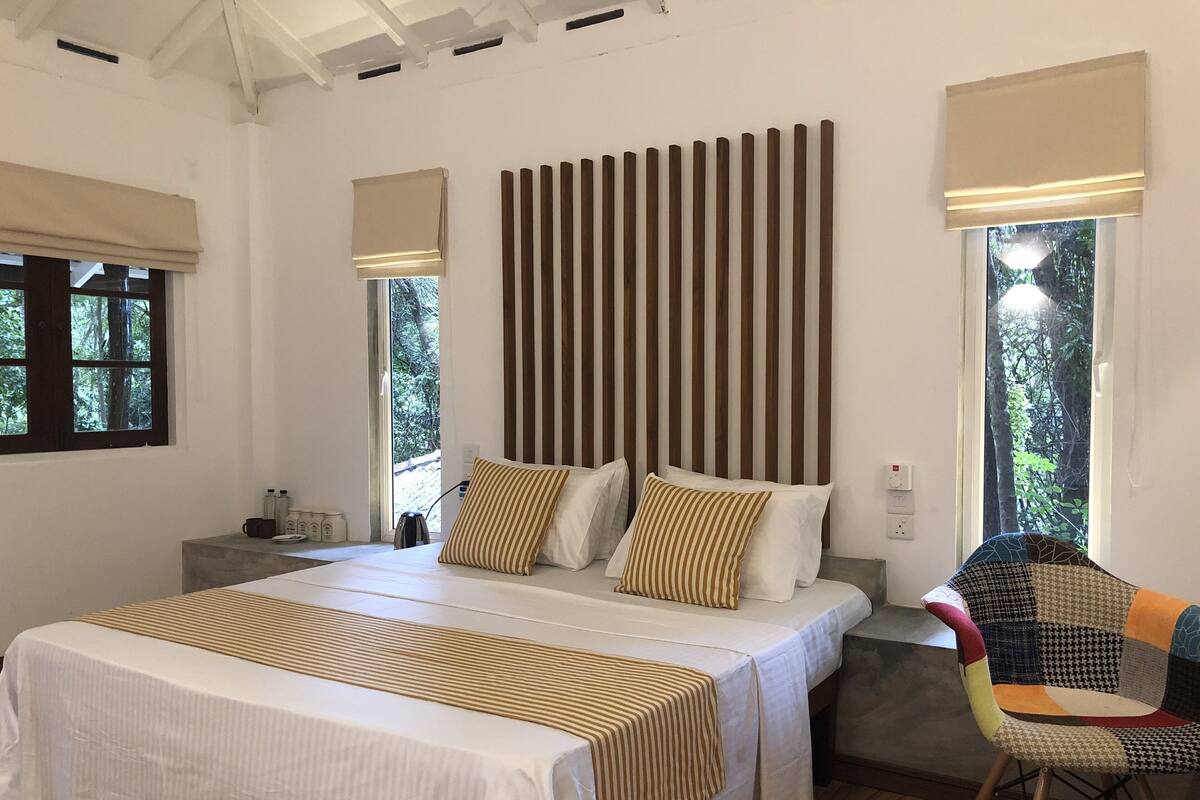 A bedroom with a large bed, a nightstand, a chair, and a window with a view of trees.