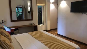 A hotel room with a large bed, a desk, a mirror, a television, and a window with a view of trees.