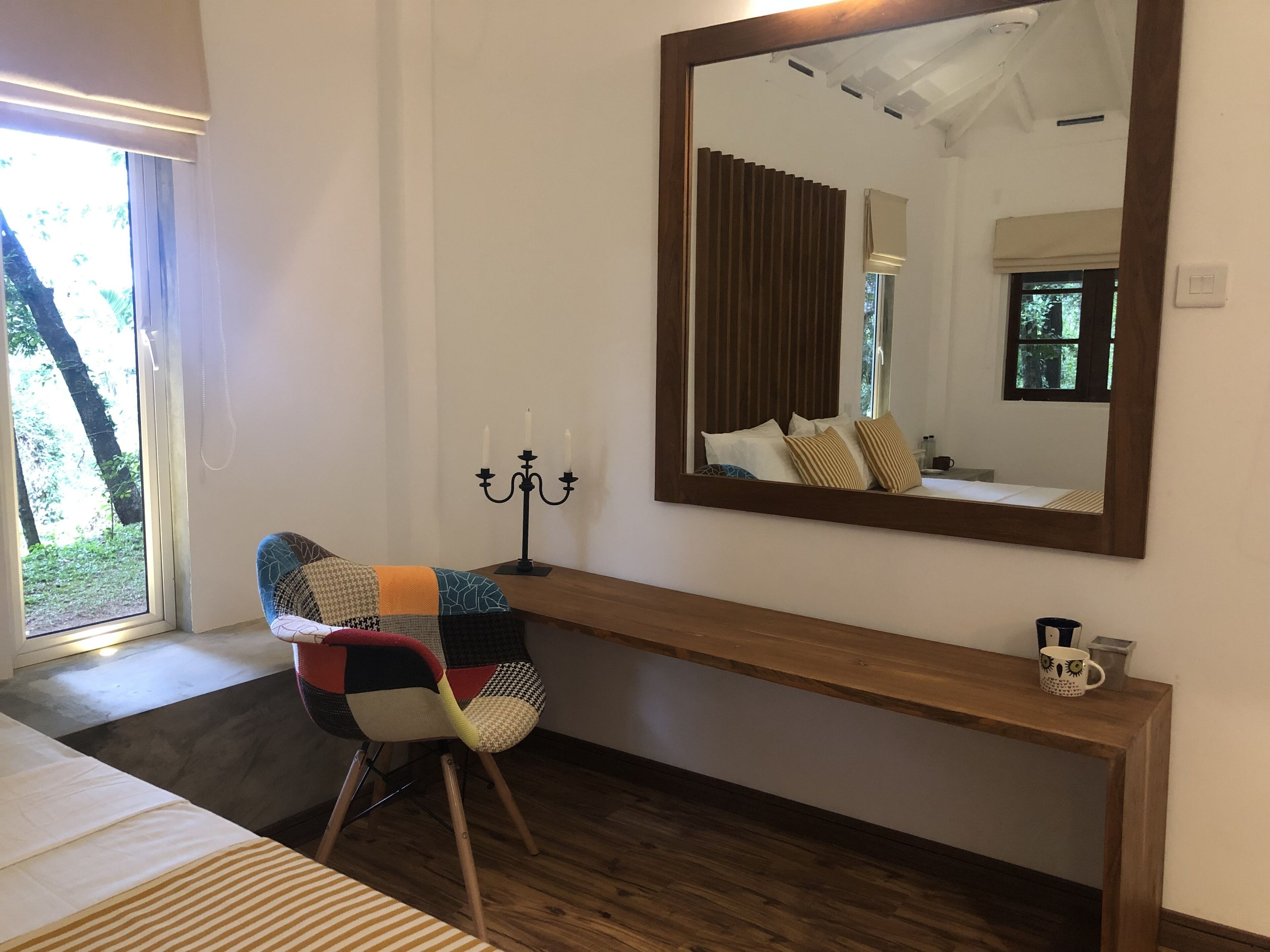 A room with a bed, a desk with a mirror, a chair, and a window with blinds.