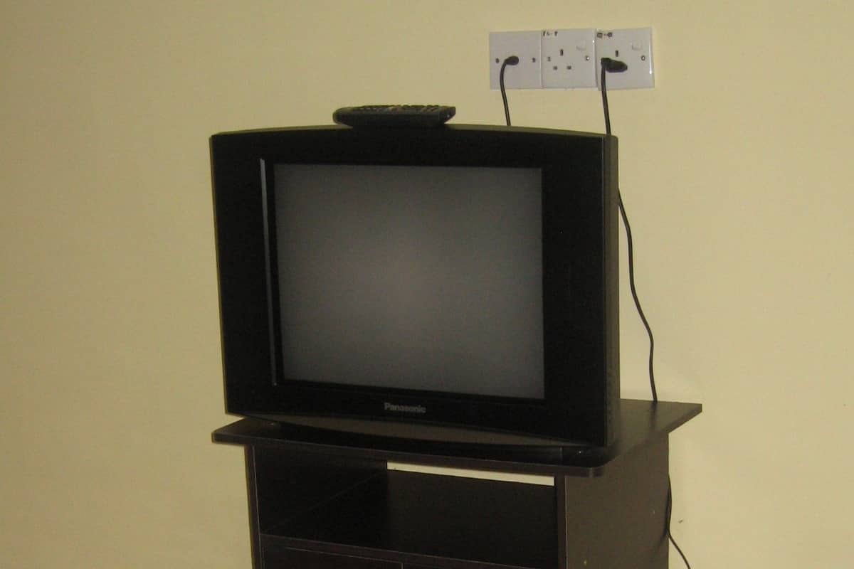 Un téléviseur posé sur un meuble en bois, avec une télécommande sur le dessus, et branché à une prise électrique au mur.