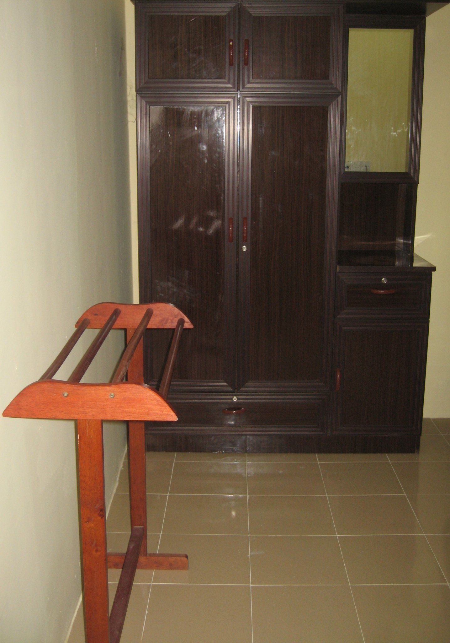 A room with a dark wooden wardrobe, a small wooden table, and a tiled floor.