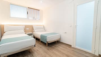 Habitación de hotel con dos camas, una ventana con persianas, suelo de madera y una puerta con vidrio esmerilado.