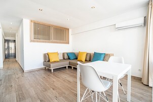 A modern living room with a sectional sofa, a dining table with chairs, and an air conditioning unit on the wall.