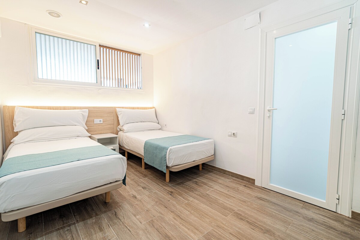 Een hotelkamer met twee bedden, een raam met zonwering, een houten vloer en een deur met glas-in-lood.