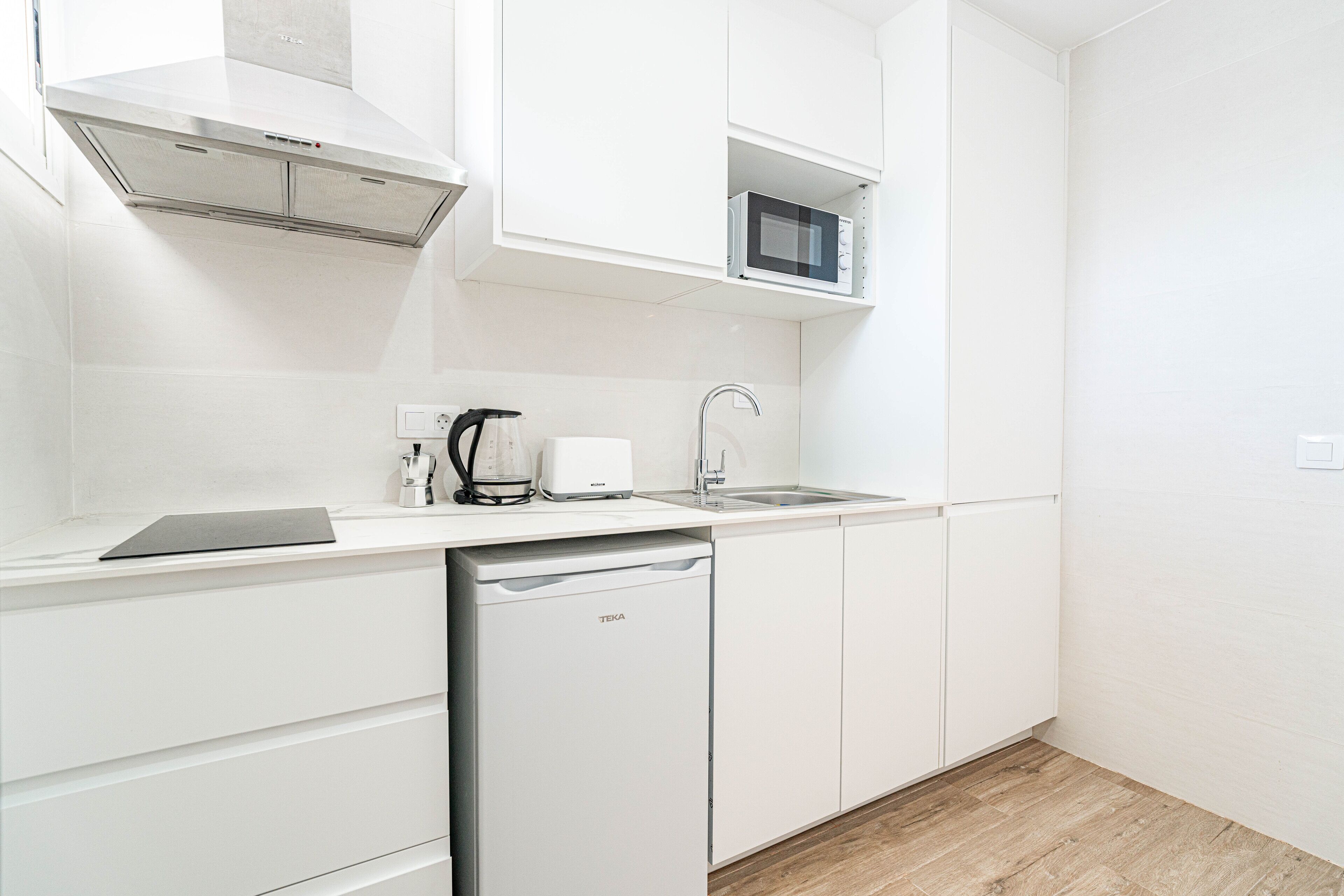 Una cocina moderna con armarios blancos, microondas integrado, lavavajillas y cafetera.