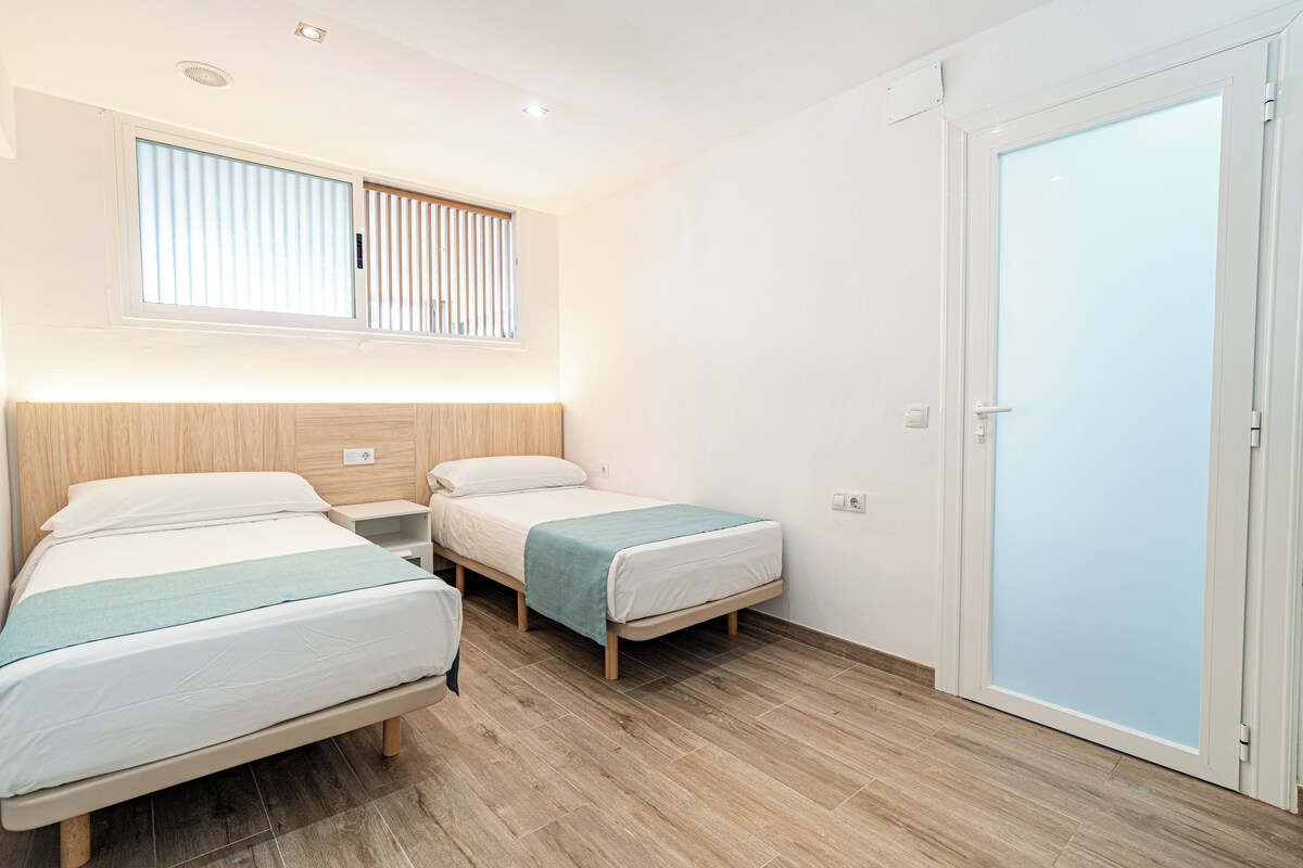 Habitación de hotel con dos camas, una ventana con persianas, cabecera de madera, armario y un interruptor de luz en la pared.
