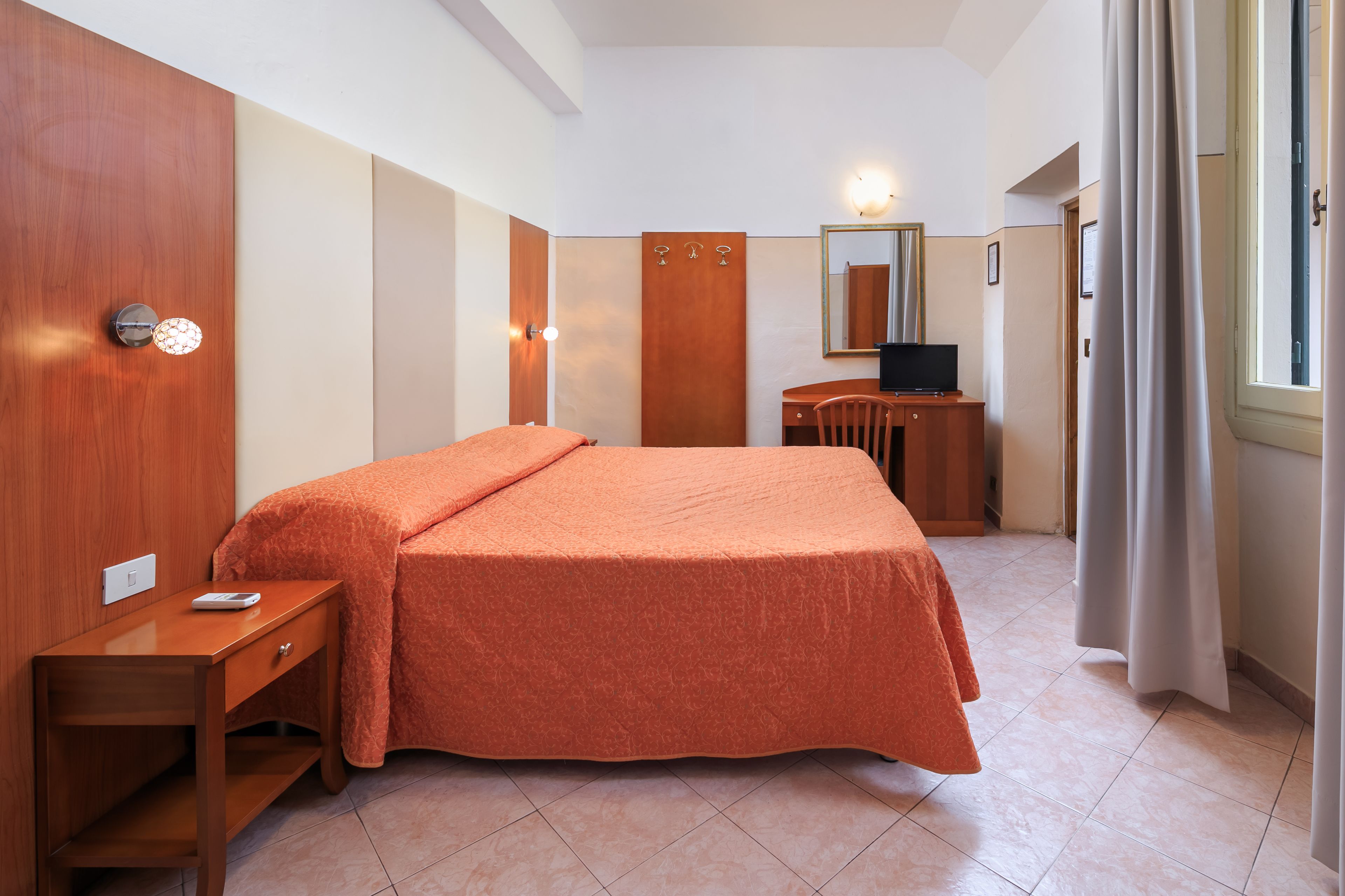 Een hotelkamer met een bed, een bureau, een stoel, een televisie en een spiegel.