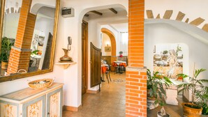 A hallway with a dining area, featuring a brick wall, a large mirror, and potted plants. - Hotel Arno Bellariva  (Florence)
