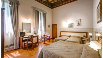 Ein Hotelzimmer mit zwei Betten, einem Schreibtisch, einem Stuhl, einem kleinen Tisch und einem Spiegel.