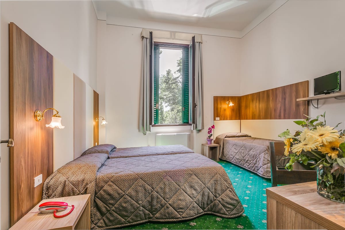 A room with two beds, a desk, a telephone, a TV, and a window with curtains.