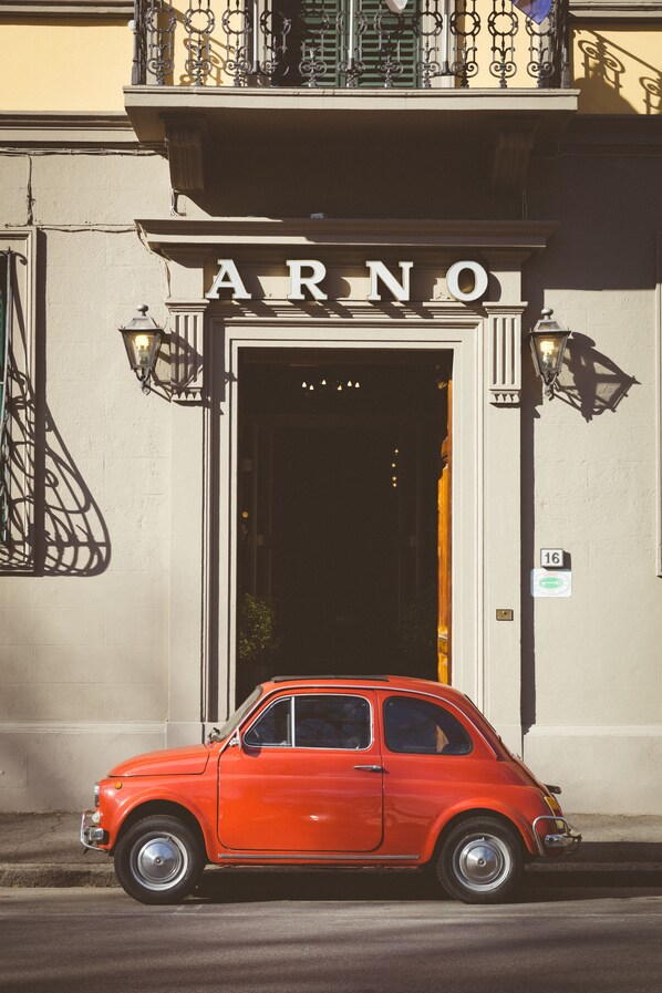 Un coche naranja antiguo estacionado frente a un edificio con un letrero que dice "ARNO".