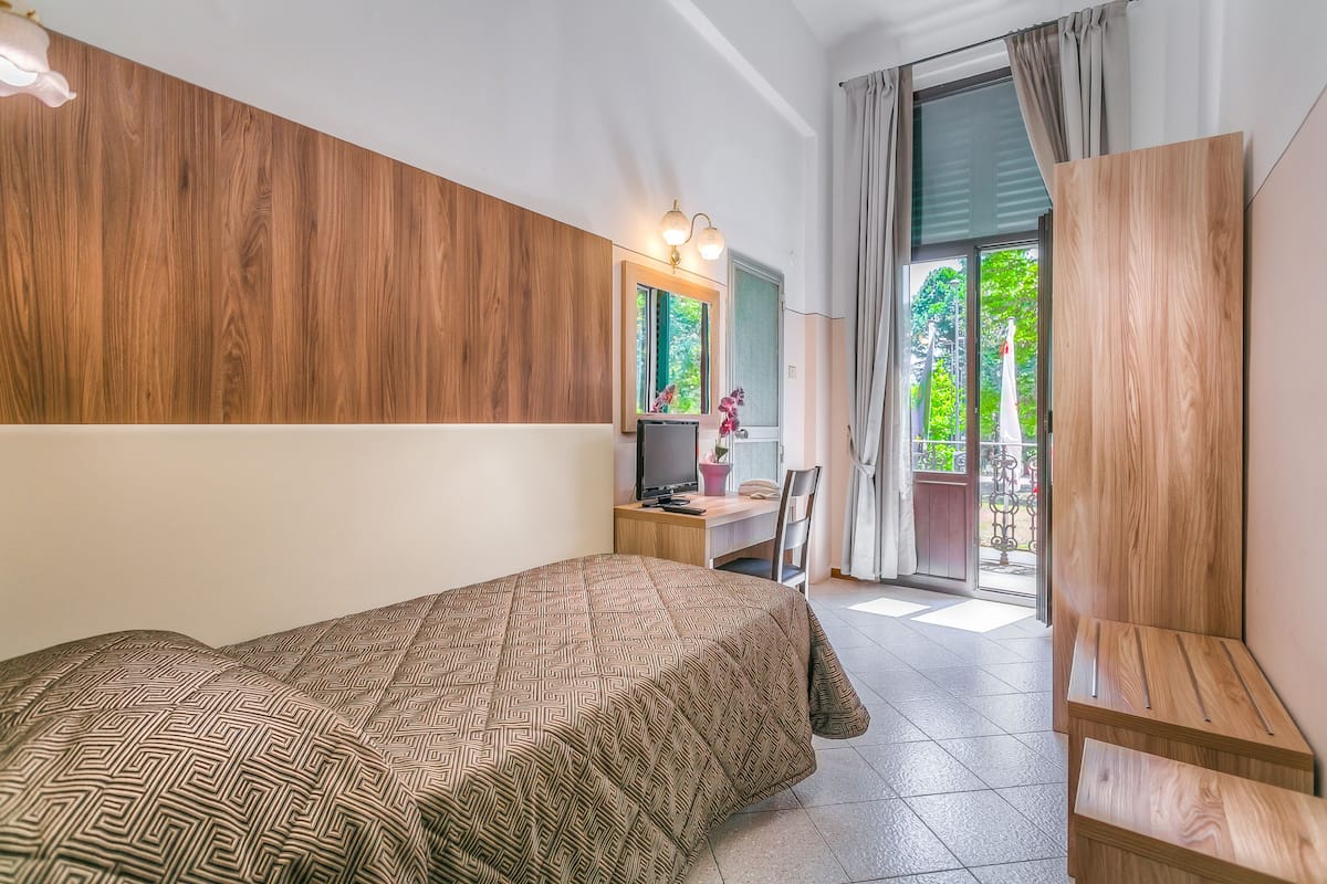 A bedroom with a bed, a desk, a chair, a TV, and a view of the outdoors.