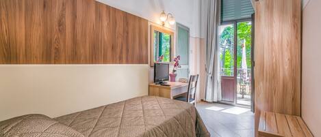 A bedroom with a bed, a desk, a chair, a TV, and a view of the outdoors.