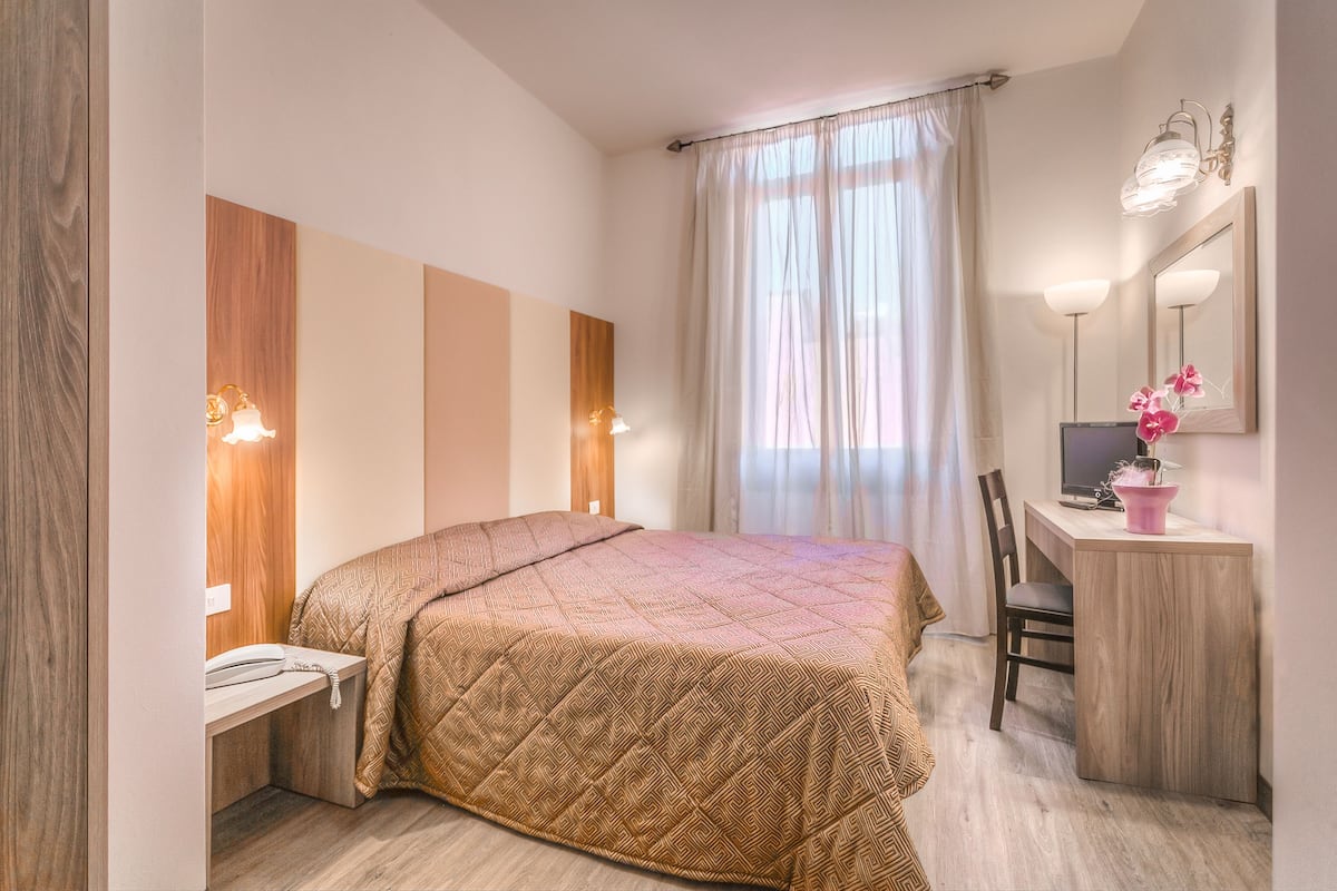 A bedroom with a bed, a desk, a chair, a mirror, and a window with curtains.