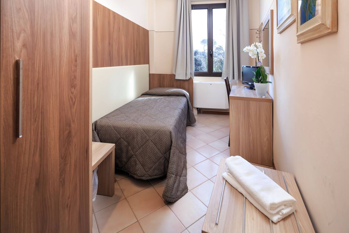 A compact bedroom with a bed, bedside table, and a small desk with a chair.