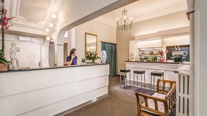 A reception area with a counter, bar stools, a chandelier, and a mirror. - Hotel Arno Bellariva  (Florence)