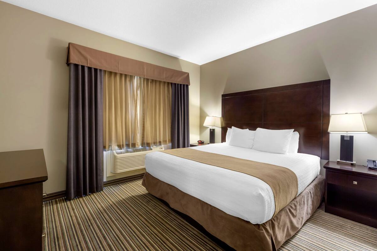A hotel room with a large bed, a desk, a nightstand, a lamp, and a window with curtains.