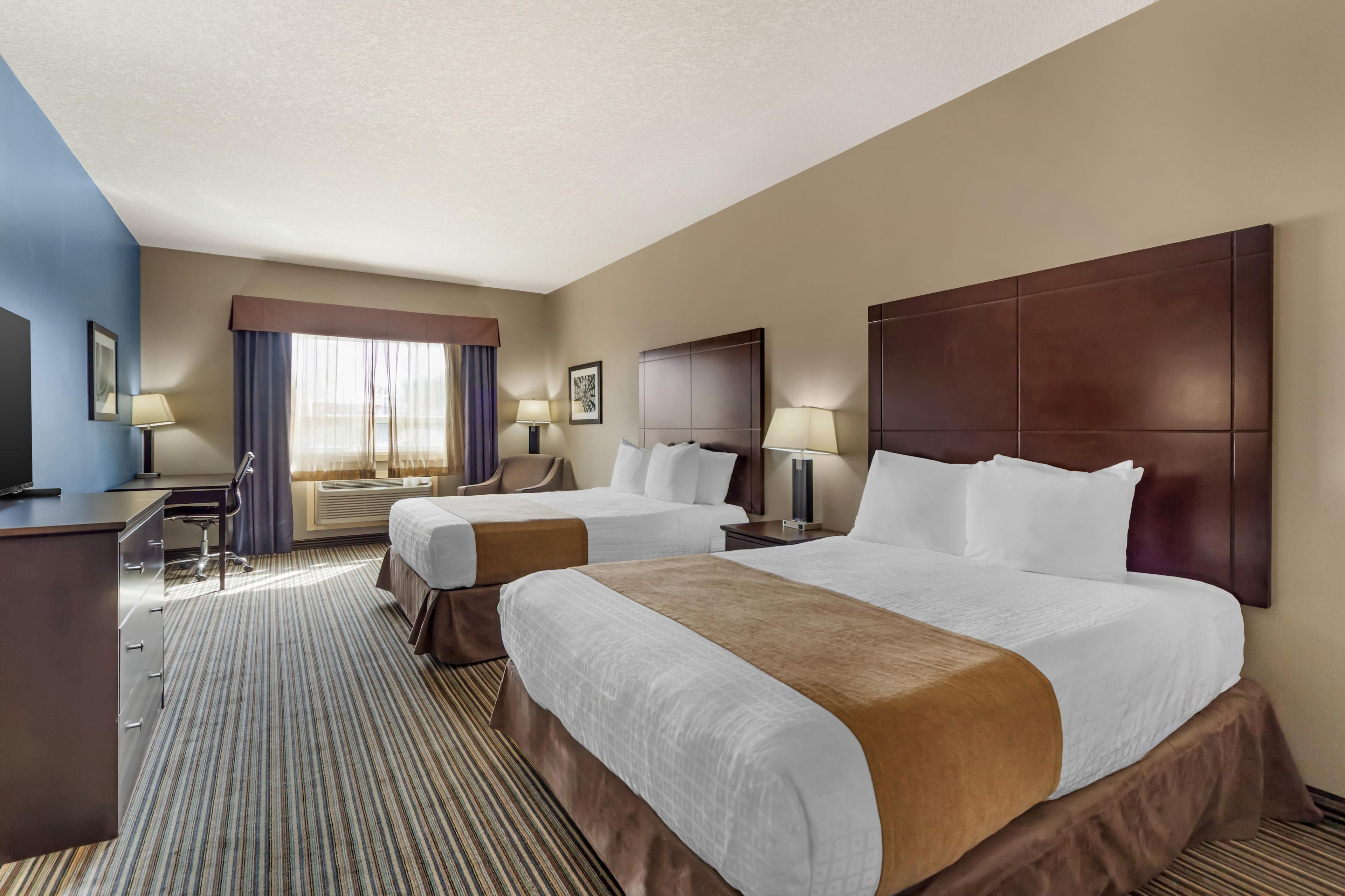 A hotel room with two beds, a desk, a chair, and a television.