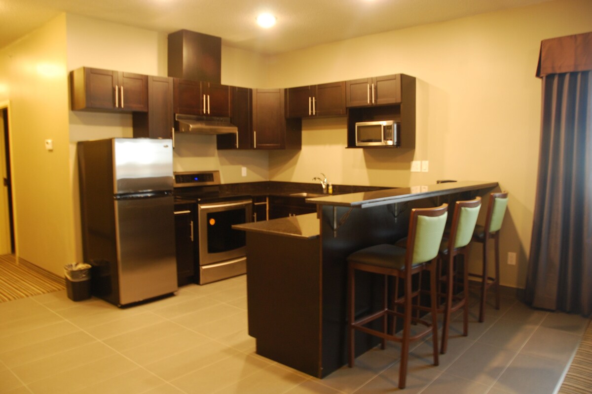 A modern kitchen with dark wooden cabinets, stainless steel appliances, and a central island with bar stools.
