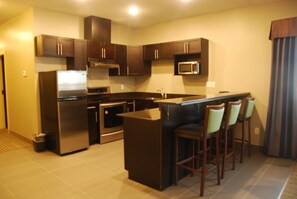 A modern kitchen with dark wooden cabinets, stainless steel appliances, and a central island with bar stools. - Best Western Plus Fort Saskatchewan Inn & Suites (Fort Saskatchewan)