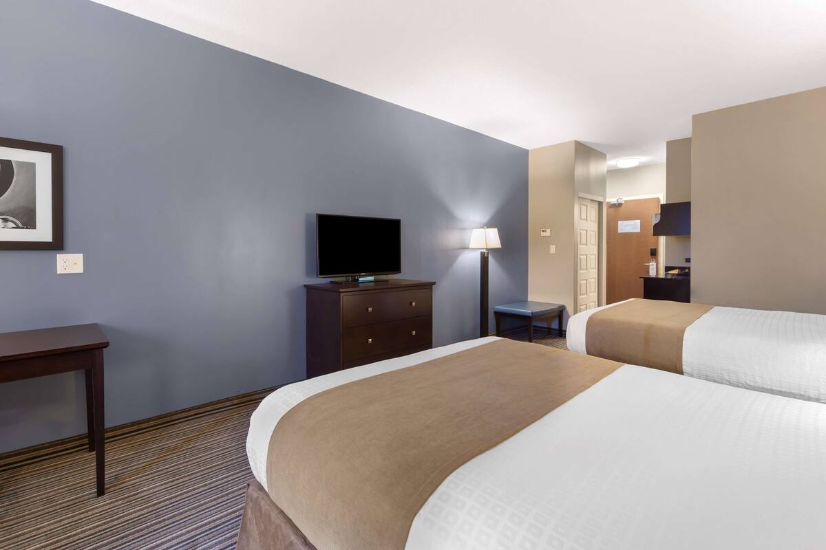 A hotel room with two beds, a desk, a television, and a lamp.