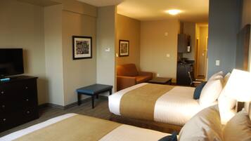 A hotel room with two beds, a desk, a chair, a television, and a kitchenette.
