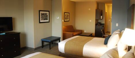 A hotel room with two beds, a desk, a chair, a television, and a kitchenette.