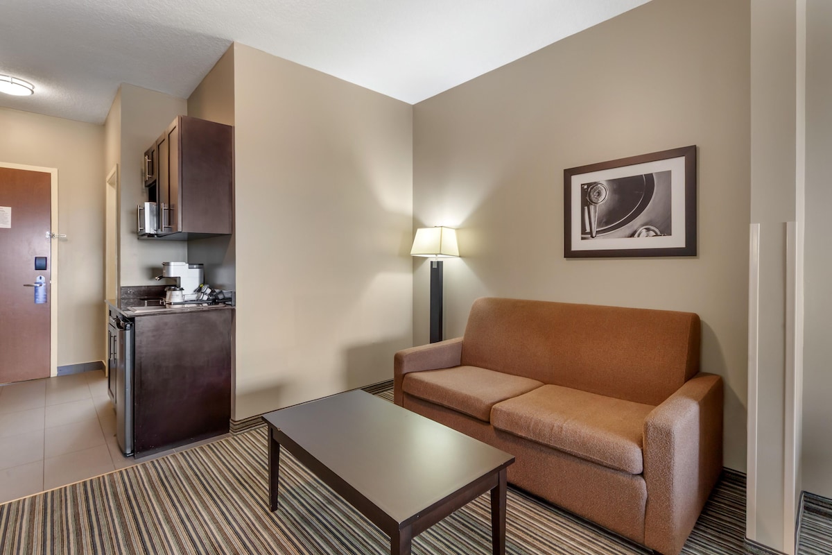Una habitación de hotel con kitchenette, un sofá, una mesa de centro y un cuadro en la pared.
