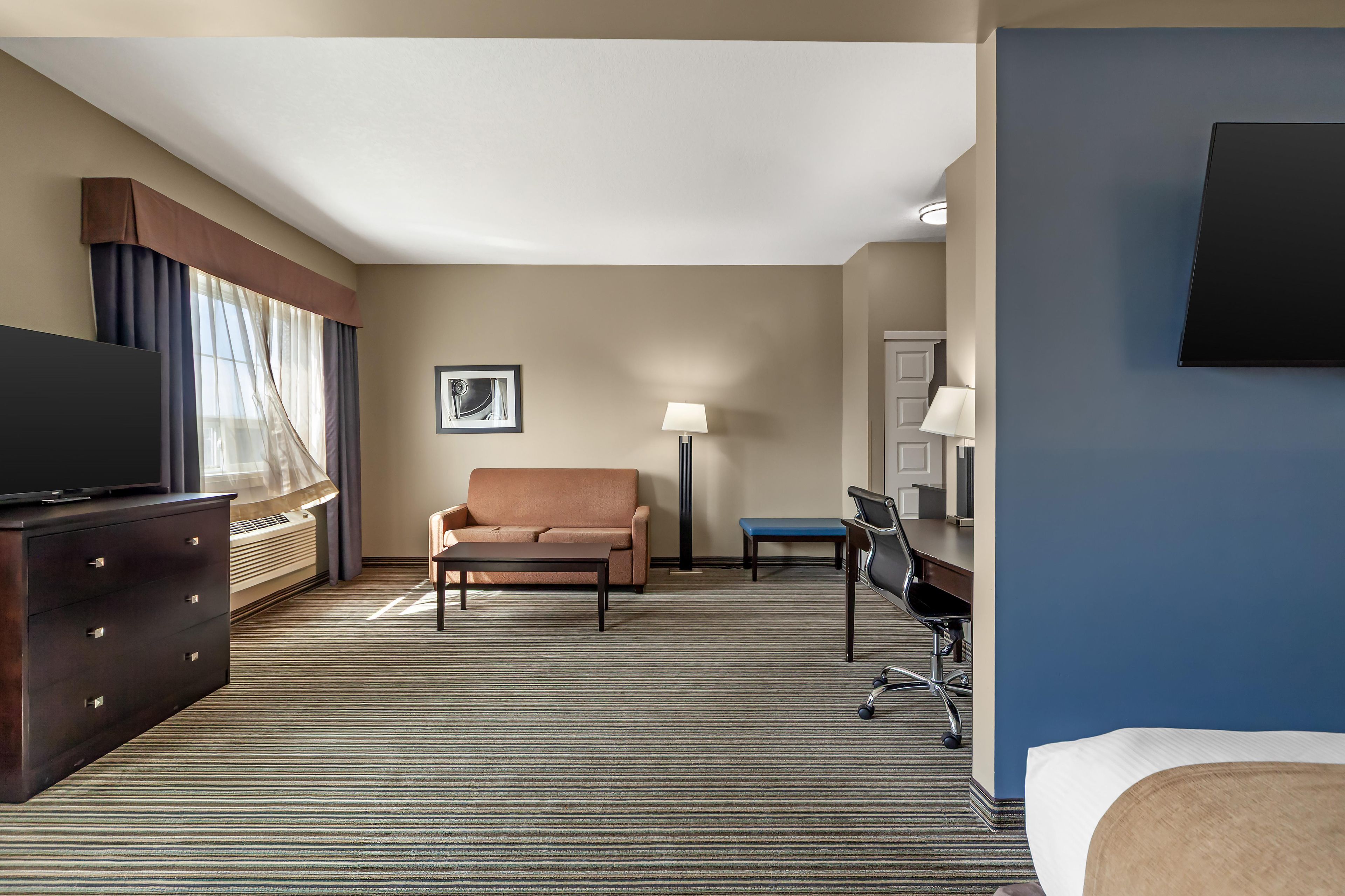 A hotel room with a flat-screen TV, a sofa, a desk with a chair, a lamp, and a bed.