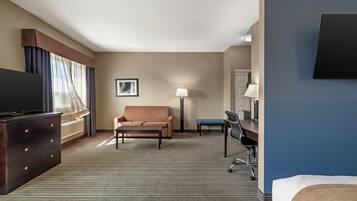 A hotel room with a flat-screen TV, a sofa, a desk with a chair, a lamp, and a bed.