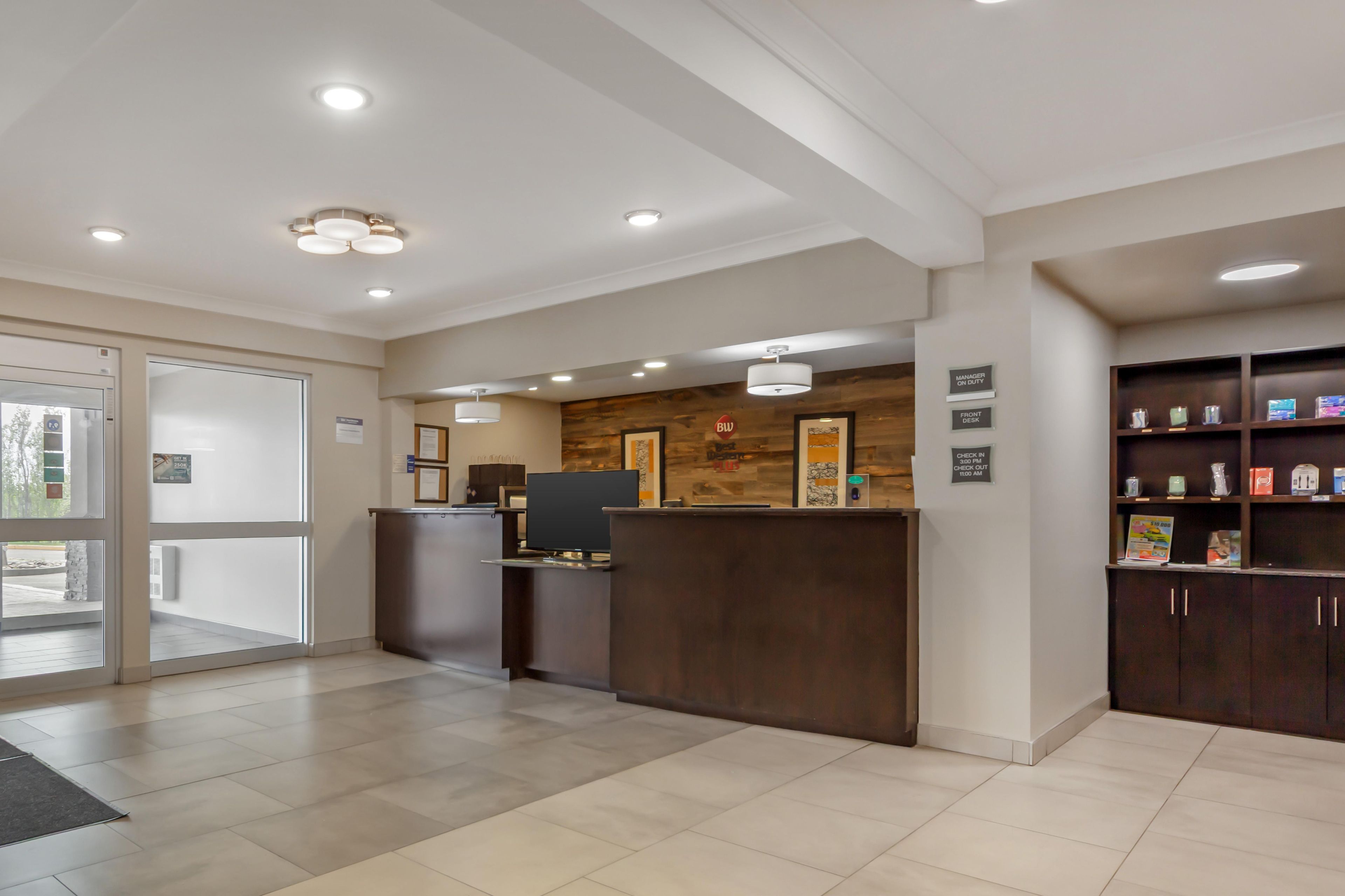 A reception area with a reception desk, a computer, and a wooden wall with artwork. There are signs indicating check-in and check-out times.